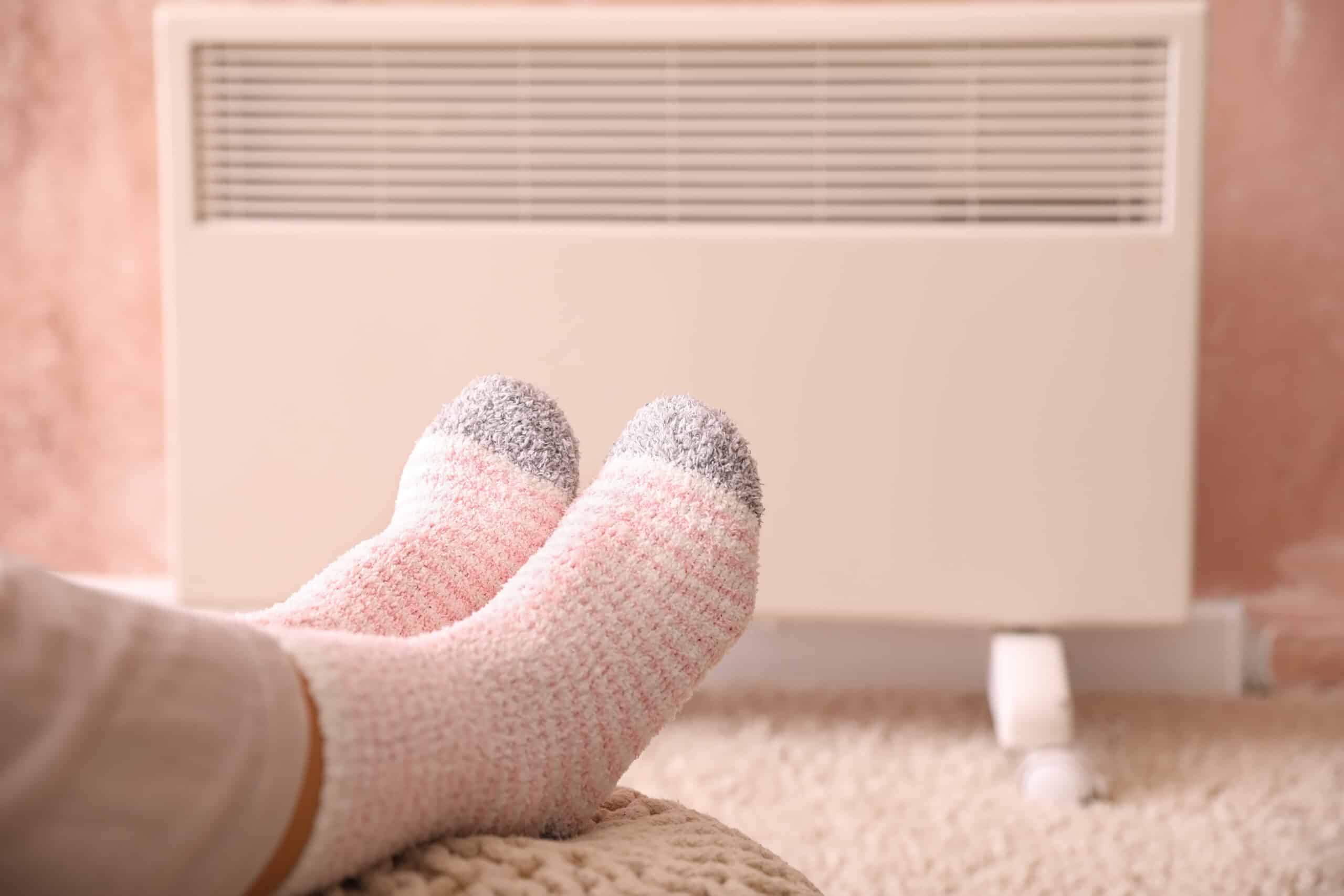 Young woman in warm socks near electric heater at home.