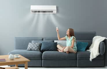 Woman adjusting mini-split air conditioner settings while sitting on a couch